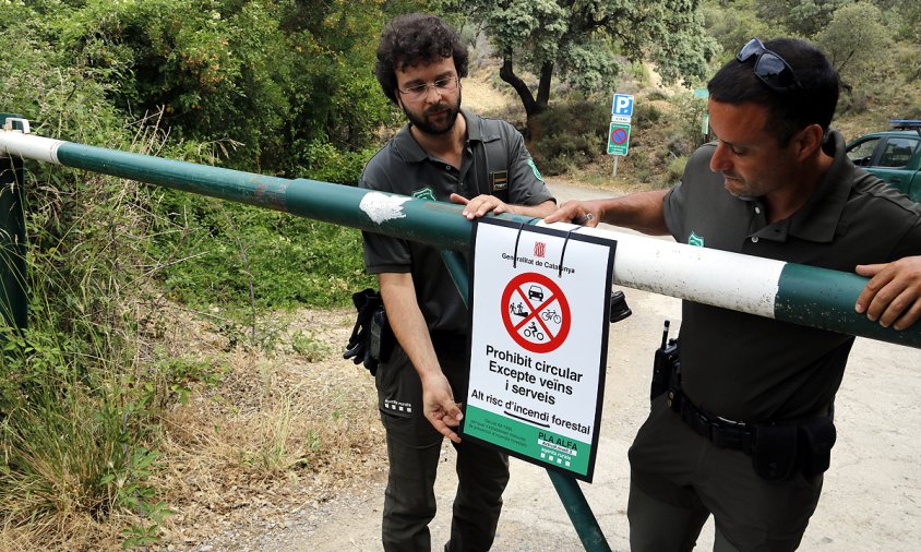 Dos Agents Rurals col·locant un cartell de prohibit el pas al Montsec, a la zona de Corçà, per l'activació del pla Alfa 3