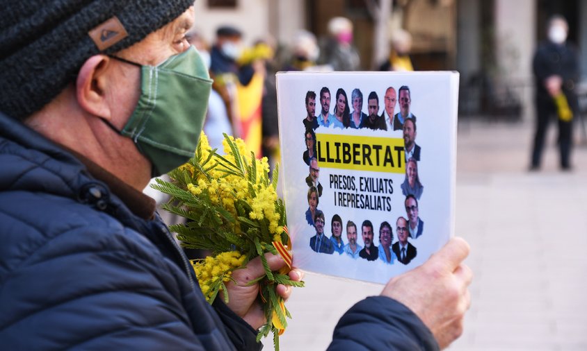 Un dels membres del col·lectiu dels Avis i Àvies amb un cartell ambs els presos i exiliats i amb una branca de mimosa, ahir a la concentració setmanal a la plaça de la Vila