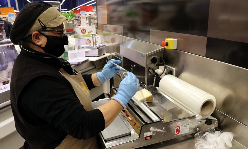 Una treballadora de l'Esclat de Malla embolica un formatge amb un paper film compostable