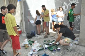 Un taller de joves pinta un mural a una de les parets exteriors de la biblioteca