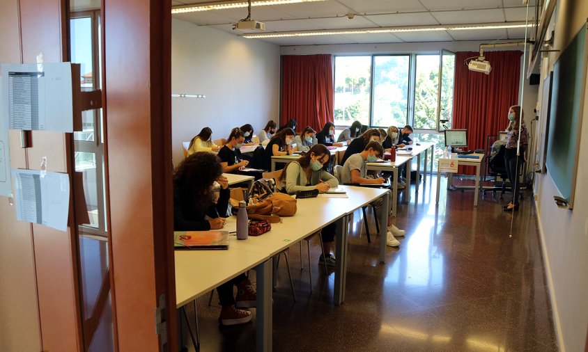 Imatge d'una aula de la URV, vista des de fora, amb alumnes fent classe amb mascareta en el primer dia del curs 2020-2021