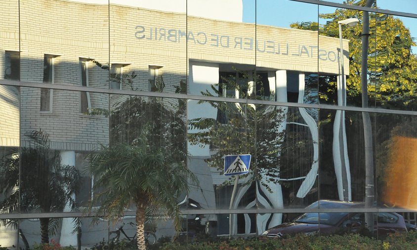 Detall de la façana de l'hospital lleuger reflectida als vidres de l'edifici consistorial