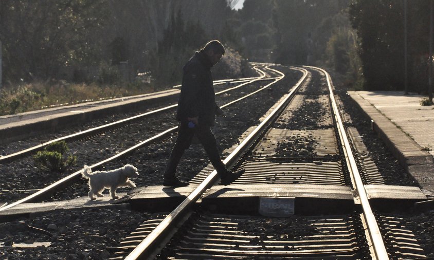 Persona travessant les vies pel pas a nivell del costat de l'antiga estació del tren